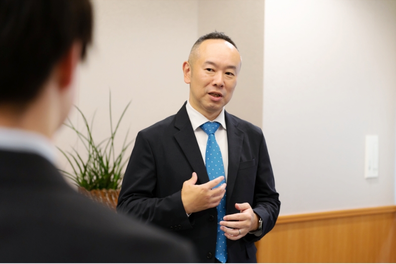 システム部 部長 向田 敬博が社員と会話している風景